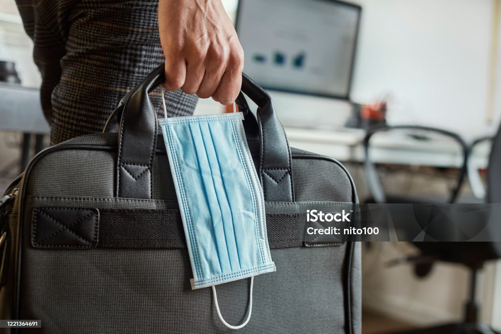 man with a briefcase and a surgical mask closeup of a young man in an office holding a briefcase and a surgical mask in his hand Coronavirus Stock Photo