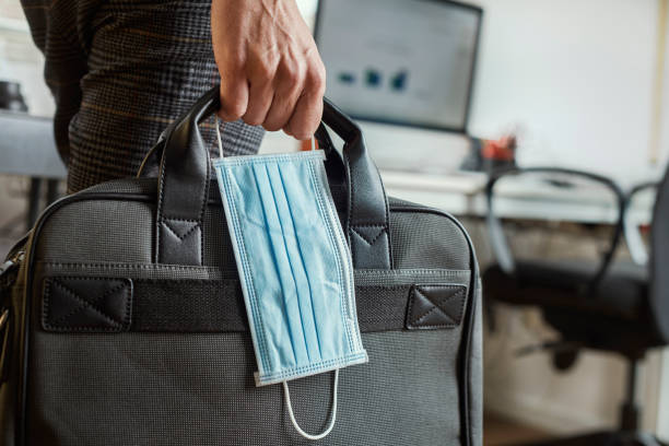 man with a briefcase and a surgical mask closeup of a young man in an office holding a briefcase and a surgical mask in his hand workplace absence stock pictures, royalty-free photos & images