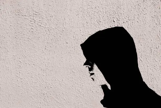 Young teenage bully boy in black hoodie with stencil effect on white wall with copy space for writing