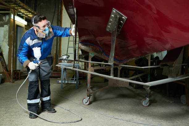 Man in Respirator Painting Boats in Customs Workshop Full length portrait of  worker wearing protective mask checking coating while painting boat in yacht workshop using paint sprayer, copy space motorboat maintenance stock pictures, royalty-free photos & images