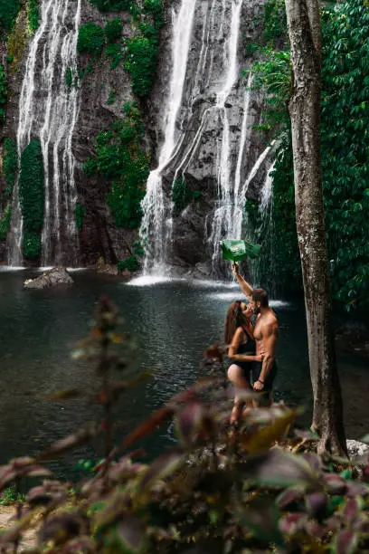 Photo of Beautiful couple at a waterfall in Indonesia. A couple in love travels around the island of Bali. A man and a woman kiss at the waterfall. Travel to Asia. Honeymoon trip. Tourists at the waterfall