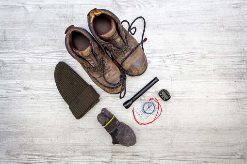 Knolling image of dirty walking boots, hat, walking socks, compass, pedometer and torch on a rough white textured board