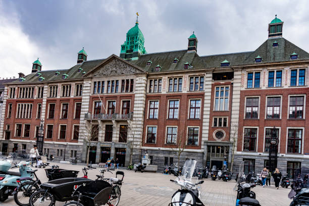 Amsterdam Stock Exchange at Beursplein 5. Amsterdam, Netherlands. There are bicycles and scooters parked outside of the red brick building with people in the background.