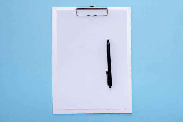 istock White clipboard and black pen with blank white paper on blue background. 1221377973