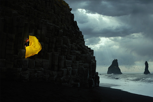 Redhead model posing in Iceland with a yellow dress, stormy background