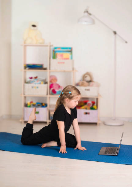 Little girl in sportswear watching online video on laptop and doing workout or fitness exercises in her room at home. Distant online training, social distance or self-isolation, online education concept. Little girl in sportswear watching online video on laptop and doing workout or fitness exercises in her room at home. Distant online training, social distance or self-isolation, online education concept. dancing school stock pictures, royalty-free photos & images