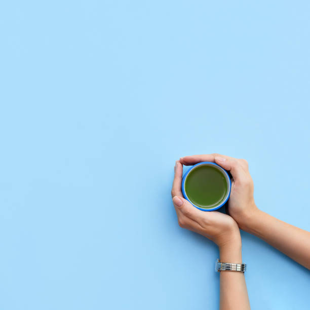 istock Woman's hands hold a cup of matcha tea on a blue background. Top view. Take away. 1221389497