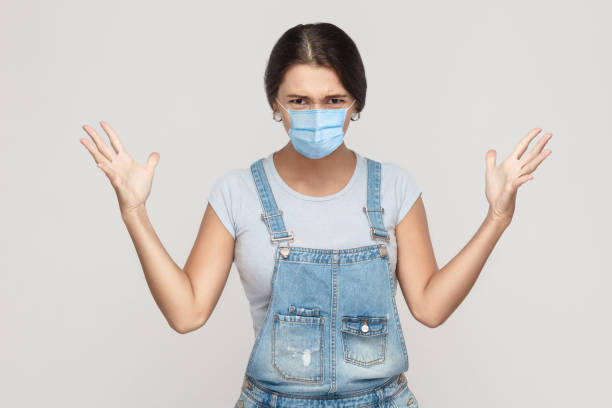 what? portrait of shocked crazy young woman with surgical medical mask in denim overalls standing, raised arms and looking at camera with angry face. - rudeness manager emotional stress asian ethnicity imagens e fotografias de stock