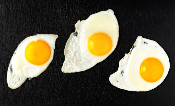 istock Three fried eggs on a black stone pan, flat lay. The concept of breakfast or lunch from fried eggs, cooking ingredients. 1221393477