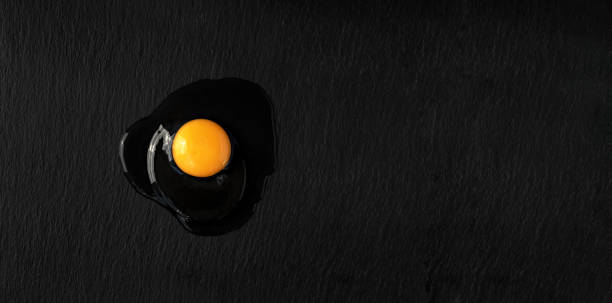 istock Fresh raw chicken egg broken on a dark stone background. Top view of a bright yolk, copy space for text or recipe. Breakfast or lunch concept 1221393480