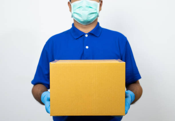 доставка человек синий форме носить резиновые перчатки и маски проведения посылки картонной коробке на белом фоне. - men mail manual worker human hand стоковые фото и изображения