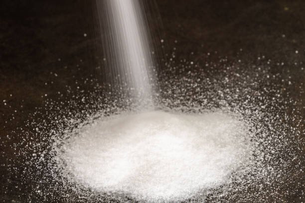Refined cane sugar powder spilling on a black table in white heap stock photo