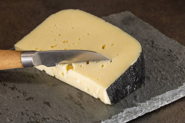 piece of Pyrenean tomme on a slate serving tray with a knife planted in cheese Photographs cooked meals gourmet French cuisine and raw ingredients ceiba tree photos stock pictures, royalty-free photos & images