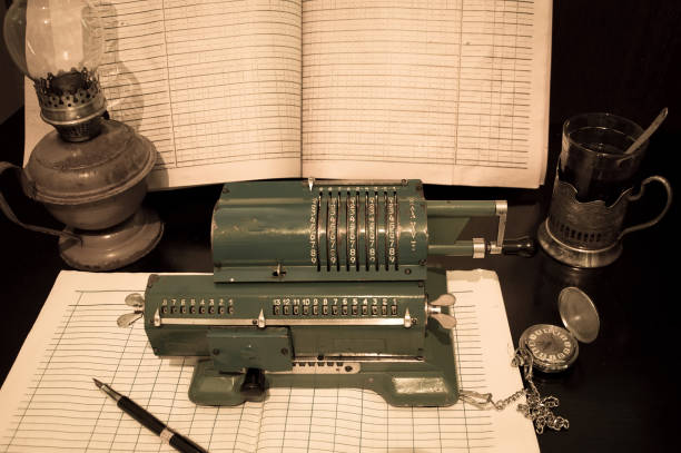An old mechanical calculator, an arithmetic counter, accounting journals, a kerosene lamp, and a pen on a black table.