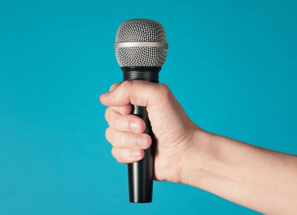 istock Hand holding up a microphone isolated against a bright blue background 1221394852