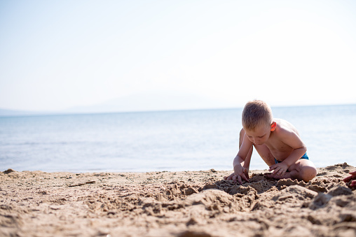Little blond boy is playing on a beach