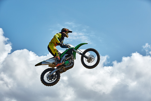 Extreme sports, motorcycle jumping. Motorcyclist makes an extreme jump against the sky. Film grain effect, illumination.