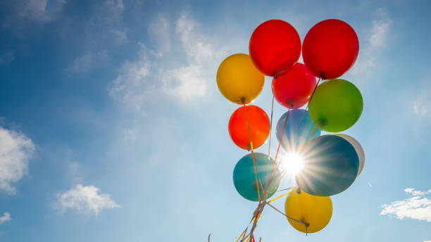 Multicoloured balloons against blue sky Low angle view of bunch of multicoloured balloons with flares against blue sky. photography balloons stock pictures, royalty-free photos & images