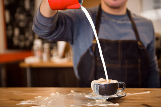 Close up barista pouring too much milk in coffee cup, making latte art