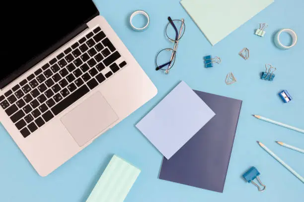 Flaylay of laptop and stationery on a blue pastel background. Workspace concept with office supplies.
