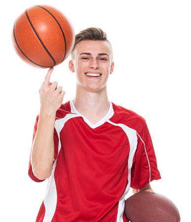 Portrait of aged 16-17 years old caucasian boys basketball player standing in front of white background wearing soccer uniform who is laughing and holding basketball - ball and playing soccer - sport and using sports ball