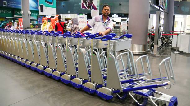 An airport crew pushes a train of luggage trolleys at the Kuala Lumpur International Airport. Kuala Lumpur, Malaysia- March 2018: An airport crew pushes a train of luggage trolleys at the Kuala Lumpur International Airport. stopover stock pictures, royalty-free photos & images