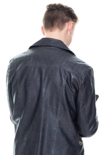 istock Caucasian young male standing in front of white background wearing leather jacket and using mobile phone 1221406250