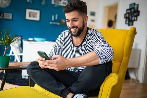 Photo of Man surfing the net and smiling while relaxing at modern living room