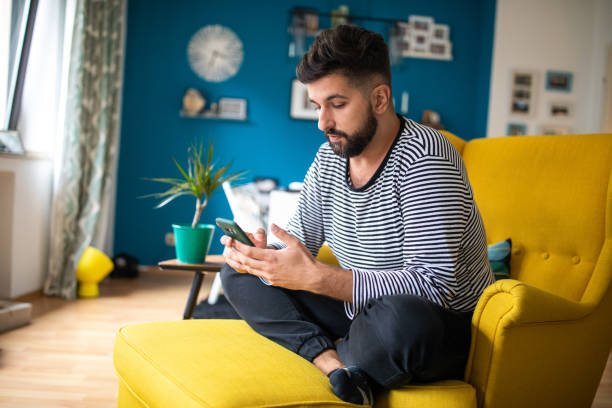 istock Man sitting on yellow armchair and using smart phone 1221410497