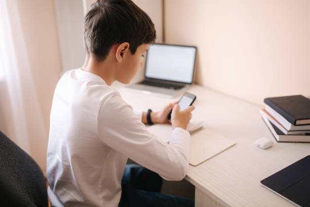 istock Schoolboy study at desk in his room. Boy use laptop and smartphone to writing in notebook. Books and tablet on the table. Study home during qurantine 1221416933