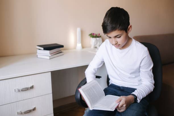 istock Young boy sitting by the desk and read the book. Study at home during quarantine 1221418254