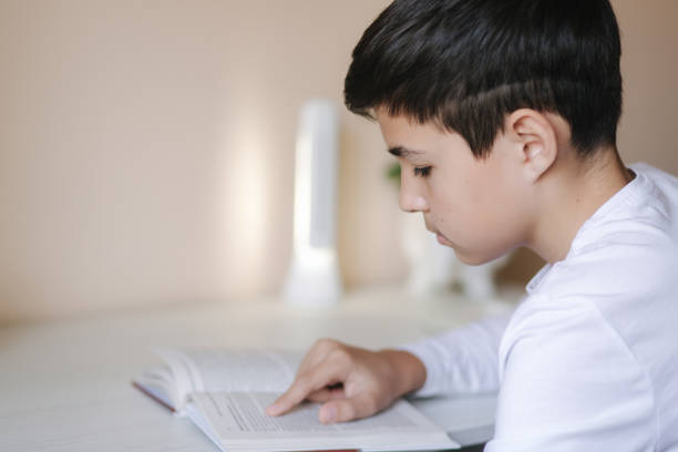 istock Young boy sitting at desk and read the book. Study at home during quarantine 1221418354