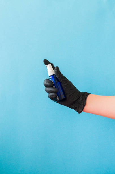 istock Hand with black gloves holding sanitizer. Blue background. 1221418998