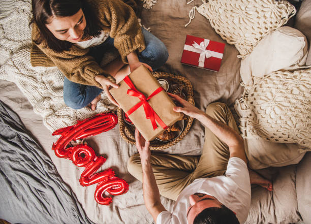 young couple sitting in bed and giving presents in boxes - rose rosé women valentines day imagens e fotografias de stock