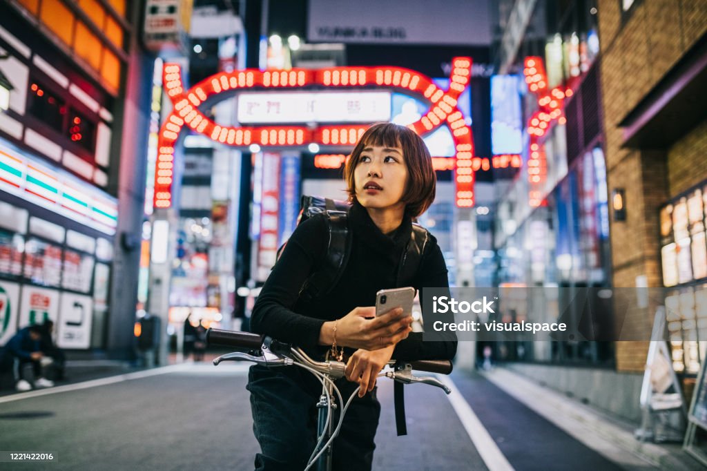 Woman Working as Bike Courier Young Asian Woman working for an food delivery app company. Using Smartphone to navigate in the big city, Japan Stock Photo