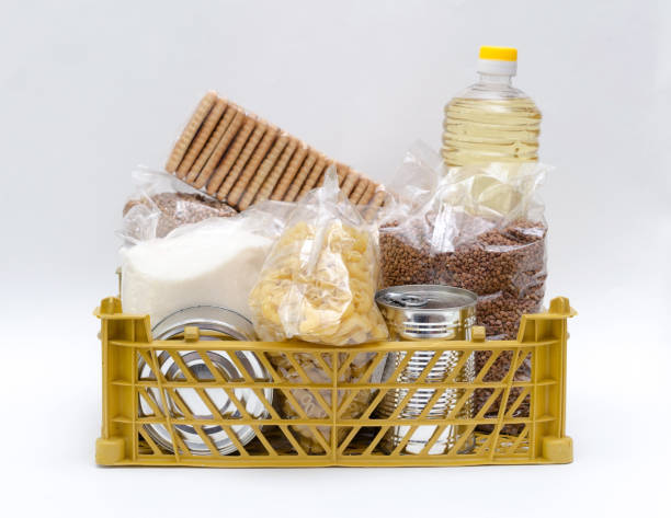 Products in packages of sugar, buckwheat, pasta, oil in a bottle in a box are on a white background. The concept of delivery of necessary products during quarantine and self-isolation. Isolate, copyspace. los productos en paquetes de azúcar, trigo sarraceno, pasta, aceite en una botella en una caja están sobre un fondo blanco. el concepto de entrega de los productos necesarios durante la cuarentena y el autoaislamiento. aislar, copiar espacio.