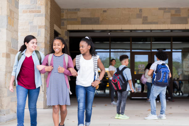 After school, three friends exit arm in arm At the end of the school day, three female friends exit arm in arm.  A mid adult female teacher supervises as all the children leave for the day. arm in arm stock pictures, royalty-free photos & images