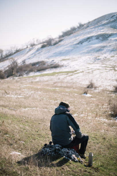 istock Back of a man sitting on a rock with snow mountain 1221437729
