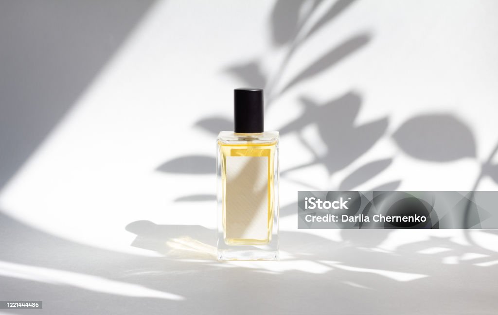 Bottle of essence perfume on white background with sunlight and shadows of leaves. Bottle of essence perfume on white background with sunlight and shadows of leaves. Minimal style perfumery template Perfume Stock Photo