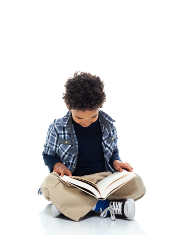 Front view of boys student sitting on floor in front of white background who is learning and holding book