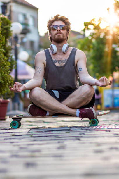 ヒッピーファッション男はヨガをやって、スケートボードでリラックス - yoga outdoors hippie people ストックフォトと画像