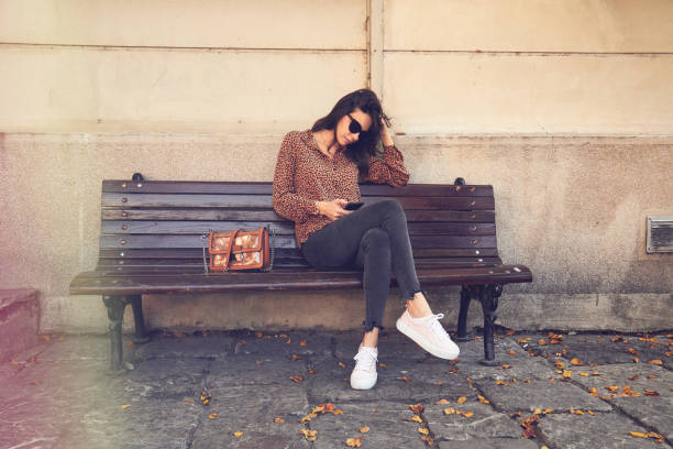 istock Pretty trendy woman using cellphone while sitting on the bench. 1221451386