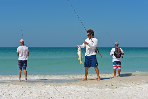 HOLMES BEACH, ANNA MARIA ISLAND, FL - May 1, 2018: A Group of Young Men on the beach Fishing in the Gulf of Mexico Enjoying a Beautiful Summer Day.