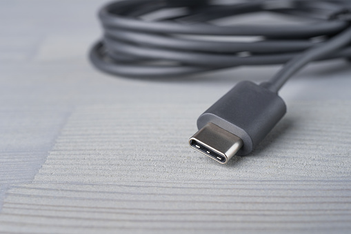 USB Type C connector with a grey cable on a wooden background. Shallow depth of field. Copy space in the bottom left corner.