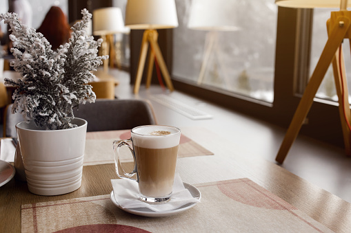 Hot latte coffee drink put on table in cafe. Coffee drink in a tall clear glass. Flat white or latte coffee art. Hipster coffee shop setting.