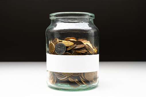 Coins in a jar with blank white label. Savings abstract concept. Copy space.