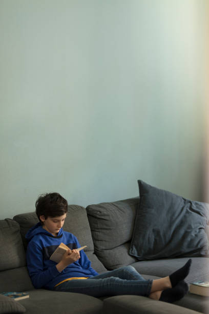 istock relaxed teenager solo reading a book seated on sofa 1221470177