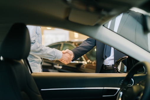 Comprador de coche estrechando la mano con el vendedor en el concesionario de automóviles, vista desde el interior del coche. photo
