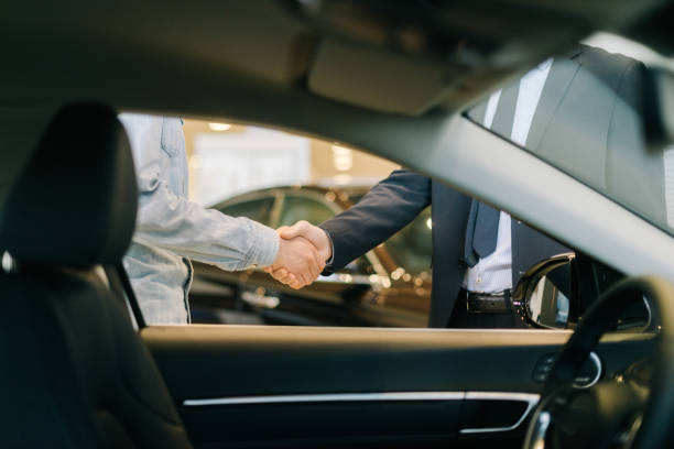 comprador de coche estrechando la mano con el vendedor en el concesionario de automóviles, vista desde el interior del coche. - selling fotografías e imágenes de stock