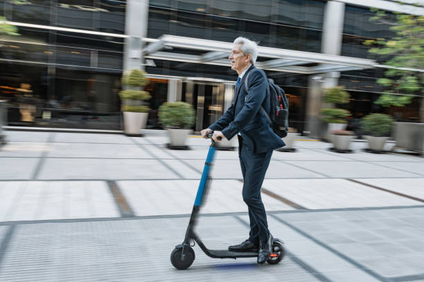 istock Mature Latino businessman in full suit riding push scooter while going to work 1221473480
